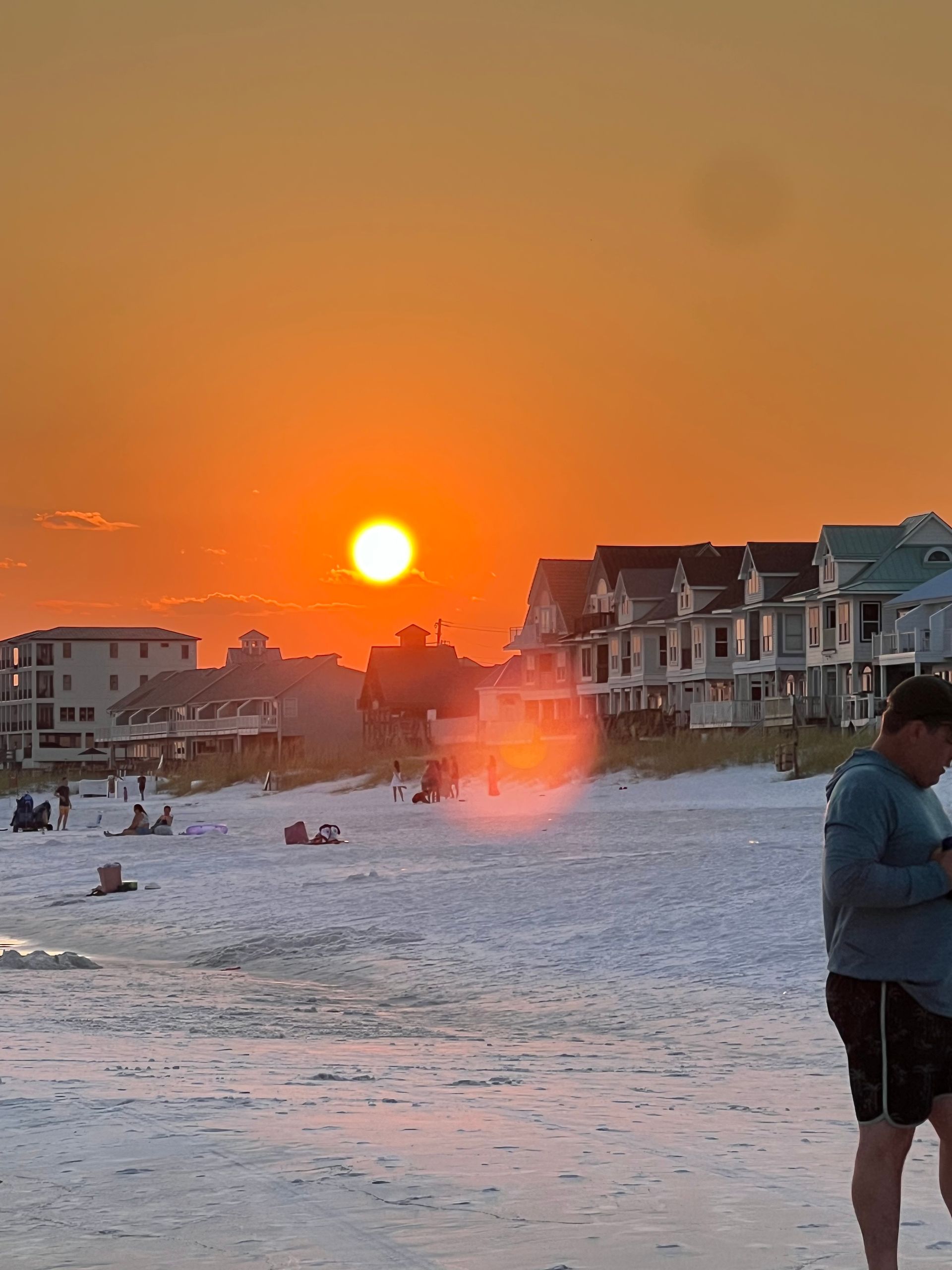 A man is standing on a beach at sunset looking at his phone