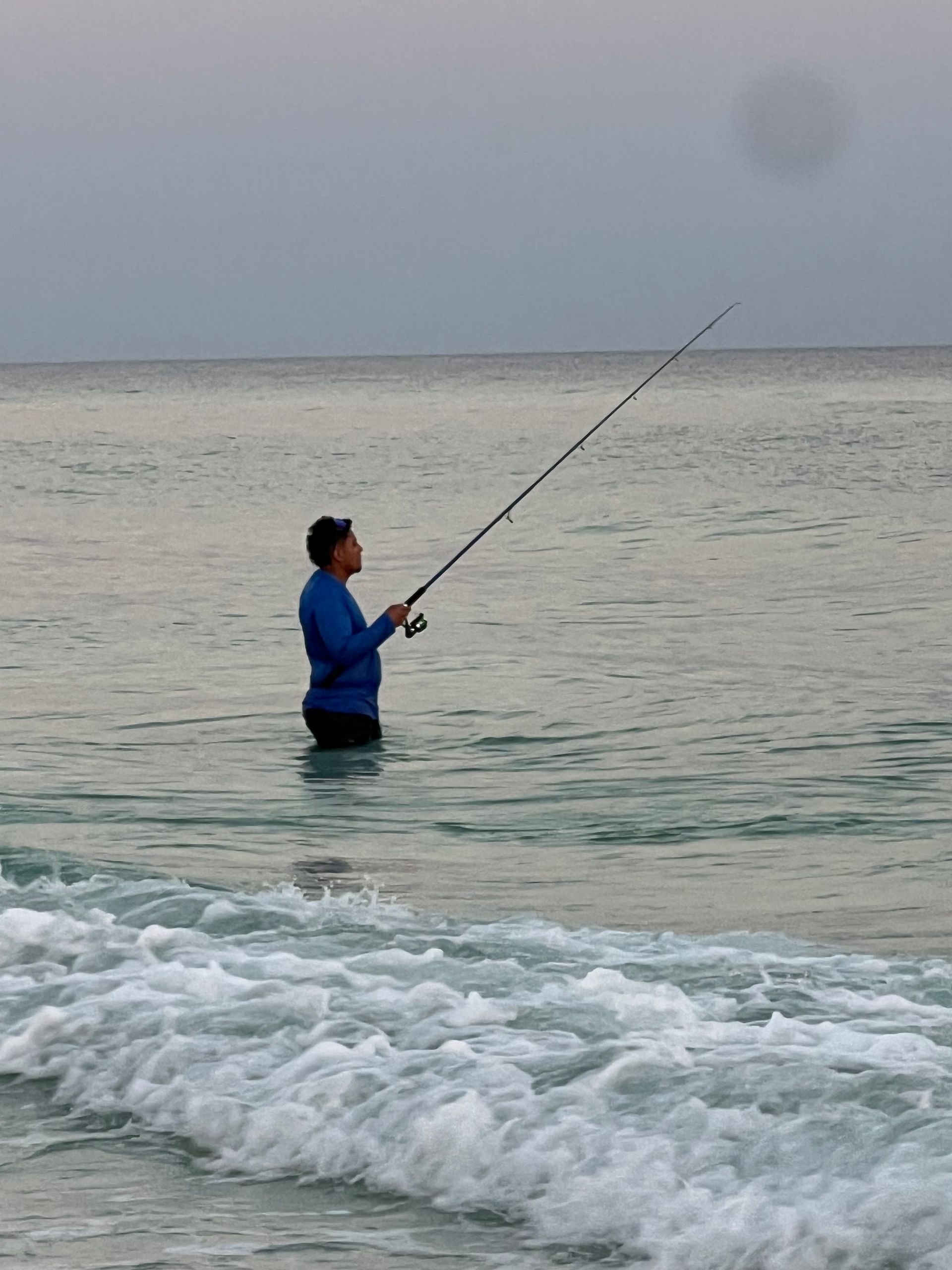 A man in a blue shirt is fishing in the ocean