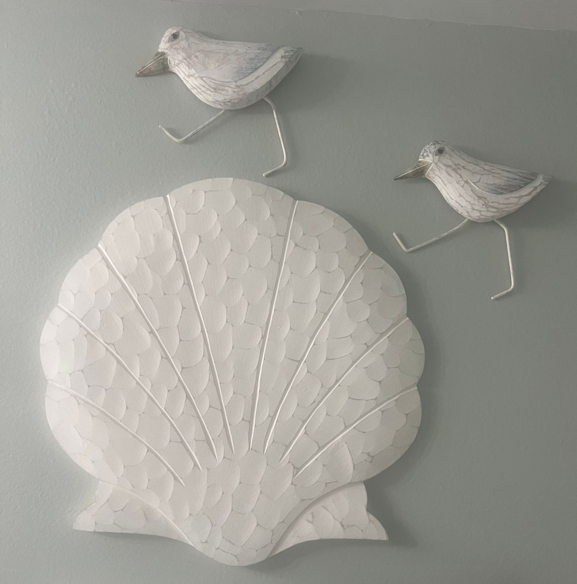 Two white birds are standing next to a white shell on a wall