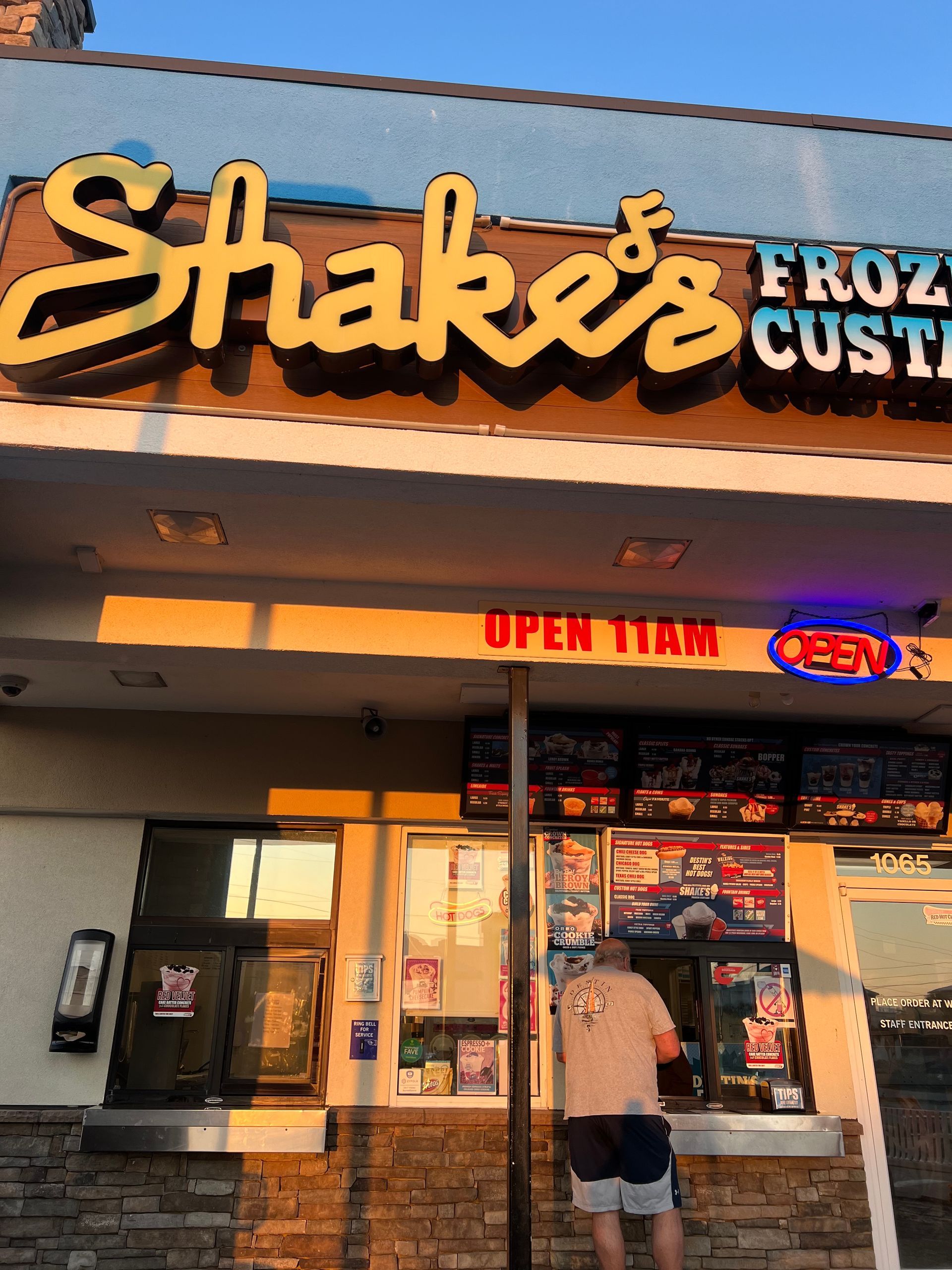 A man standing in front of a shake 's frozen custard restaurant