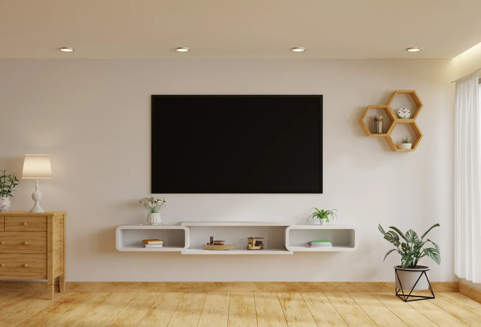 Living room with a large TV, floating shelf, wooden floor, and decorative plants.