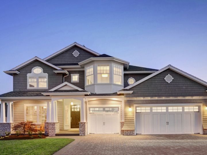 Two-story house with beige siding, white trim, and a brick driveway, illuminated at dusk.