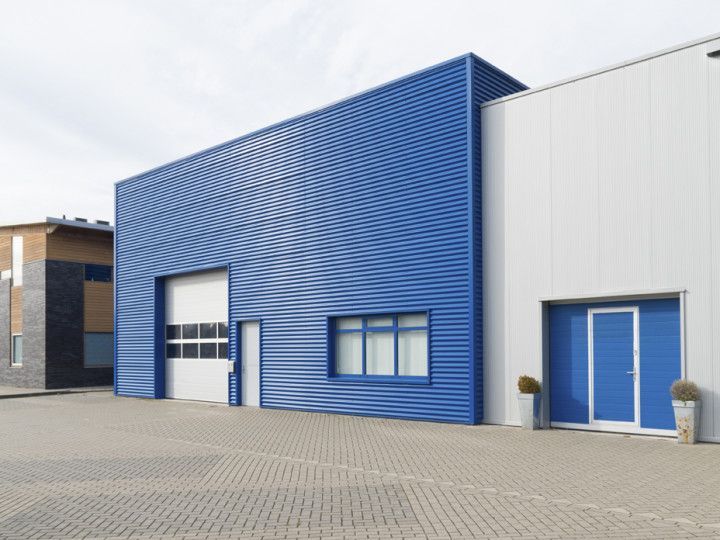 Blue and white industrial buildings with garage and door, on paved lot.