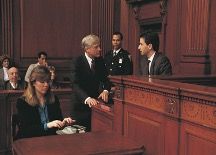 A man and a woman are sitting at a table in a courtroom talking to each other.