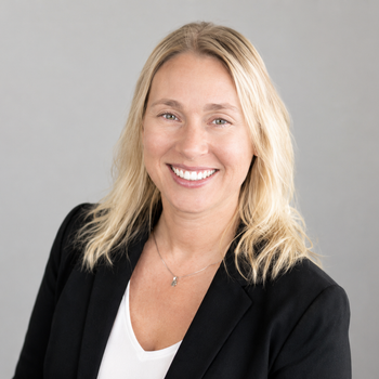 Smiling blonde woman in a black blazer against a light gray background