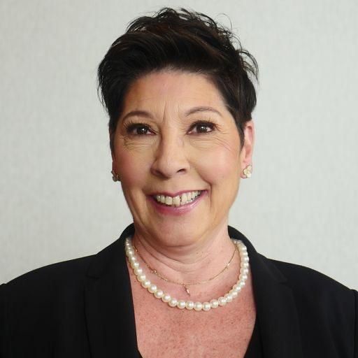 a woman wearing a pearl necklace and a black jacket is smiling .