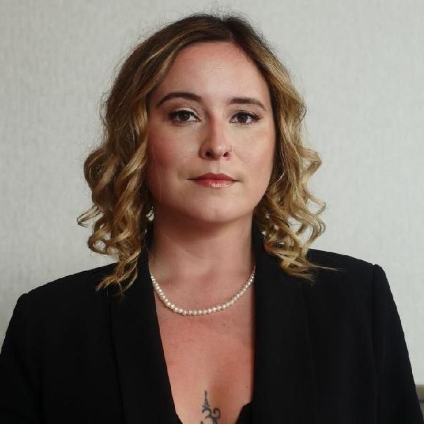 a woman wearing a pearl necklace and a black jacket is smiling .