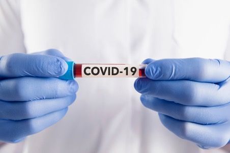 A person wearing blue gloves is holding a test tube with the word covid-19 on it.
