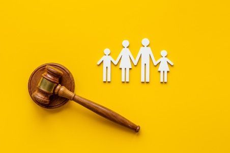 A wooden gavel and paper cut outs of a family on a yellow background.