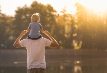 a father standing, with his son sitting on his shoulders