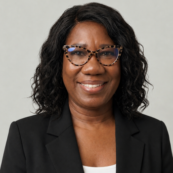Portrait of a smiling woman in a black blazer and glasses against a light gray background