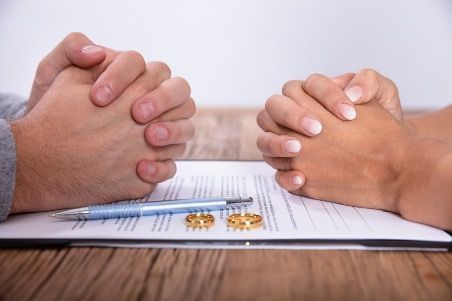 A man and a woman are sitting at a table with their hands folded.