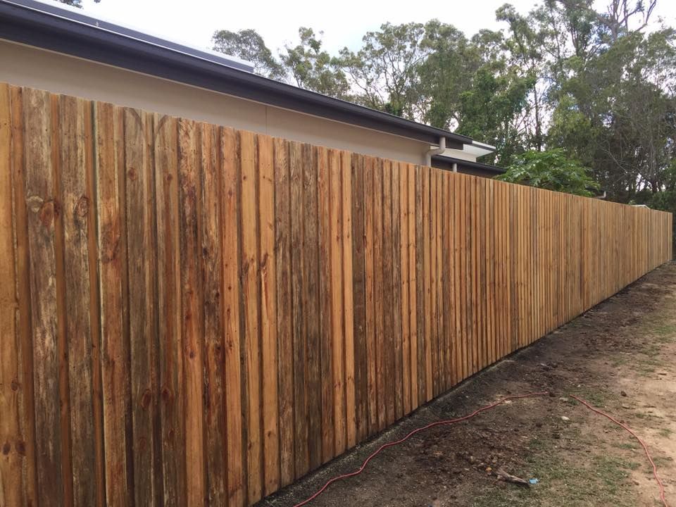 Long wooden privacy fence stretching beside a house along a dirt path