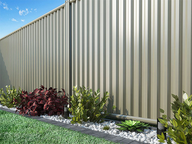 Corrugated metal fence beside a landscaped strip with rocks and red and green plants