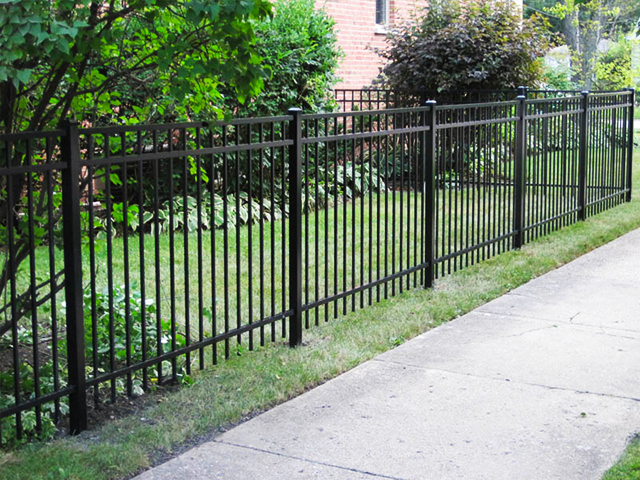 Black metal fence beside a sidewalk with green shrubs and trees in a residential area