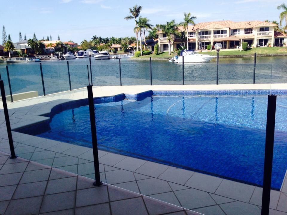 Blue-tiled pool overlooking a calm canal with boats, palm trees, and waterfront homes in the background