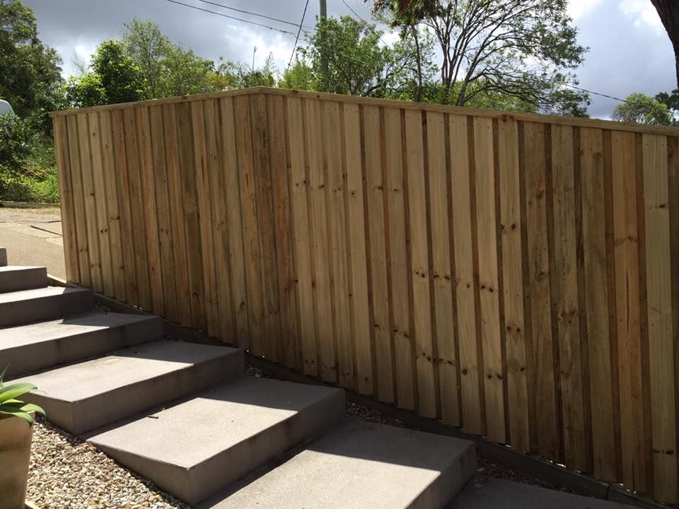 Wooden fence beside outdoor concrete steps, with trees and cloudy sky in the background