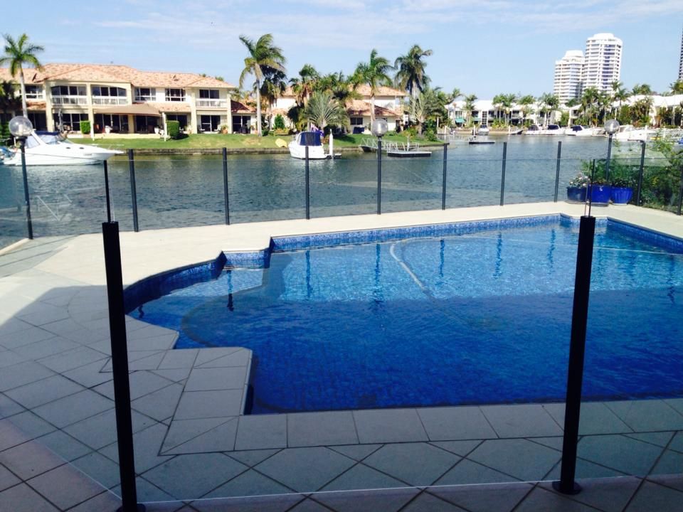 Blue swimming pool overlooking a marina with palm trees, condos, and a clear sky