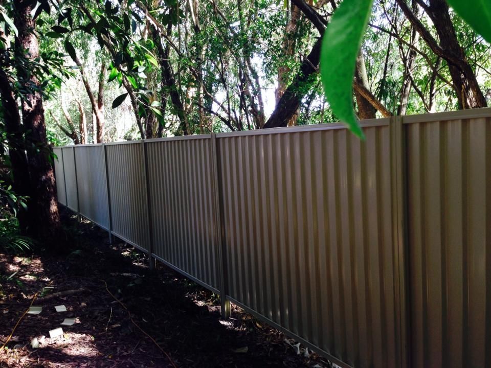 Long corrugated metal fence along a shaded wooded path with trees overhead