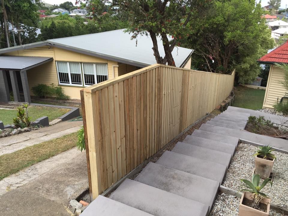 Concrete steps beside a tall wooden fence on a sloped residential walkway