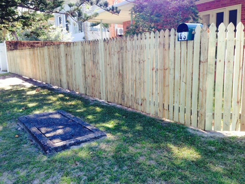 A wooden fence beside a grassy yard, with a house and mailbox in the background.
