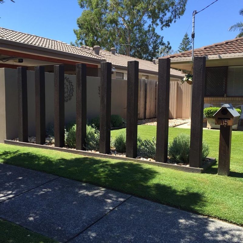 Suburban courtyard with vertical wooden fence panels, green lawn, and tiled roofs in bright sunlight