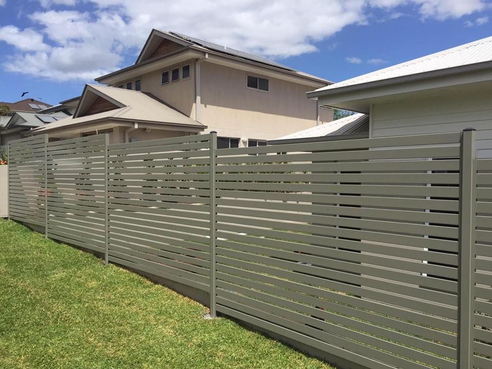 Gray horizontal-slat fence along a grassy yard with suburban houses and cloudy sky in the background