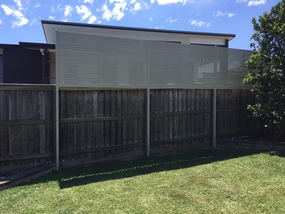 Backyard with wooden fence, green lawn, and a beige house under a blue sky