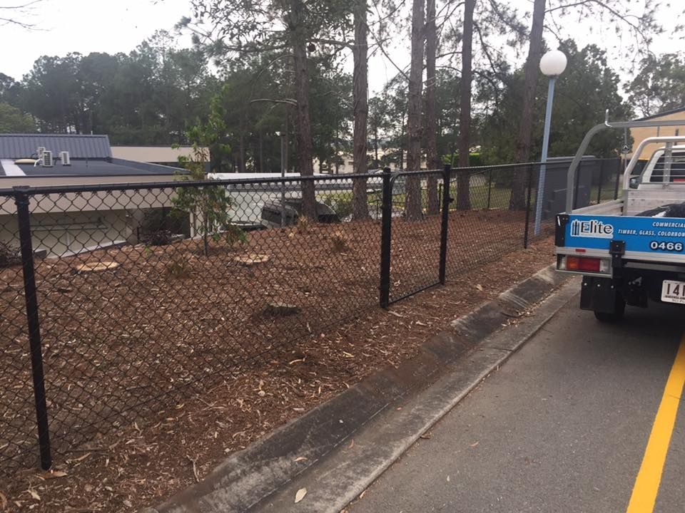 Chain-link fence beside a road with a blue utility truck parked at the curb