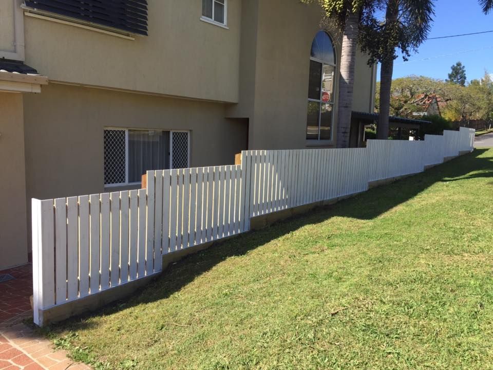 White picket fence along a grassy slope beside beige apartment buildings.