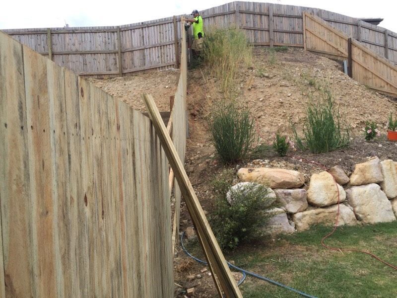Steep backyard slope with wooden fences, rocks, and a person in a bright green shirt at the top