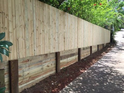 Wooden fence beside a paved path, with greenery and sunlight casting shadows לאורך the roadside.