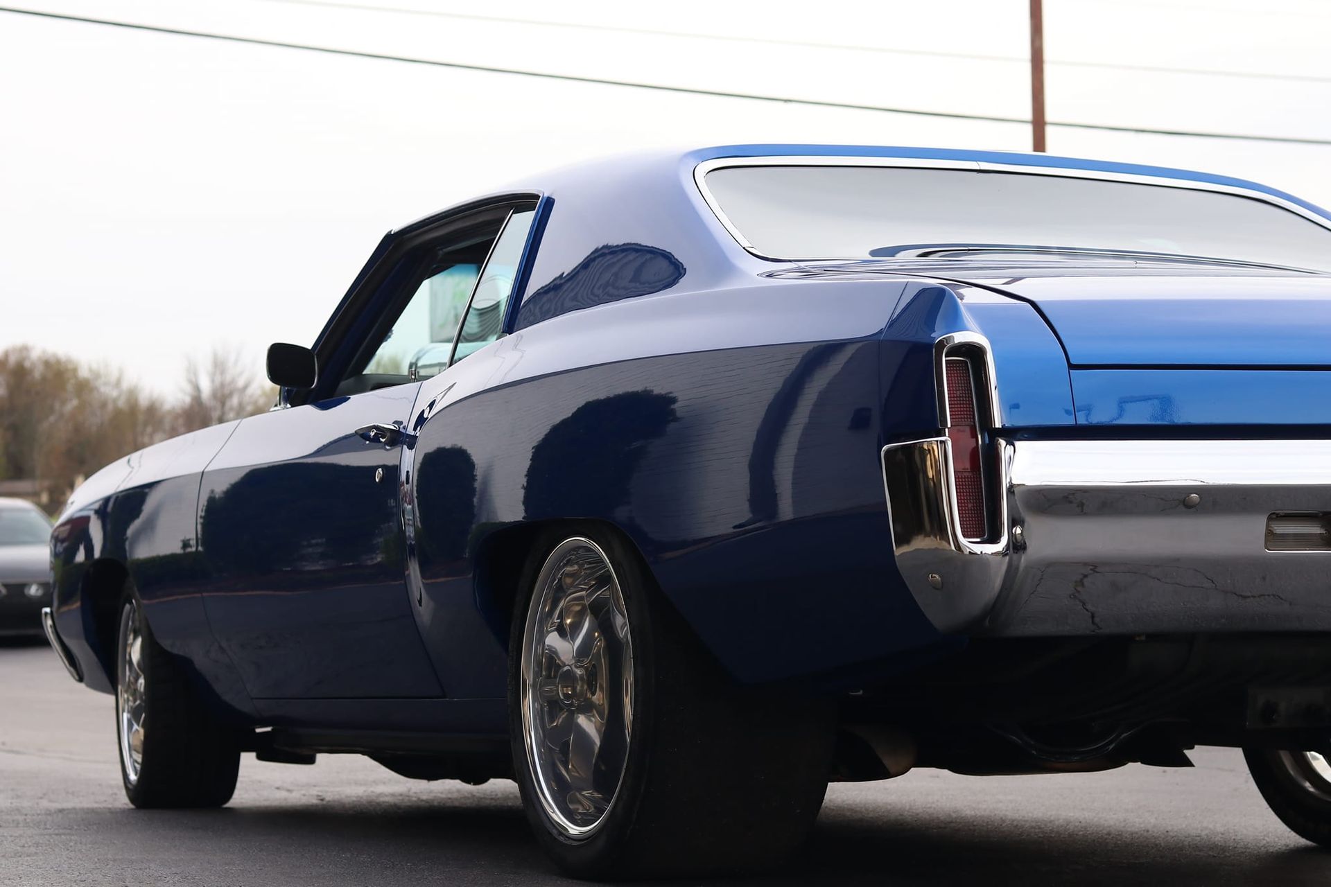Blue classic car, rear view, chrome wheels, parked on asphalt.