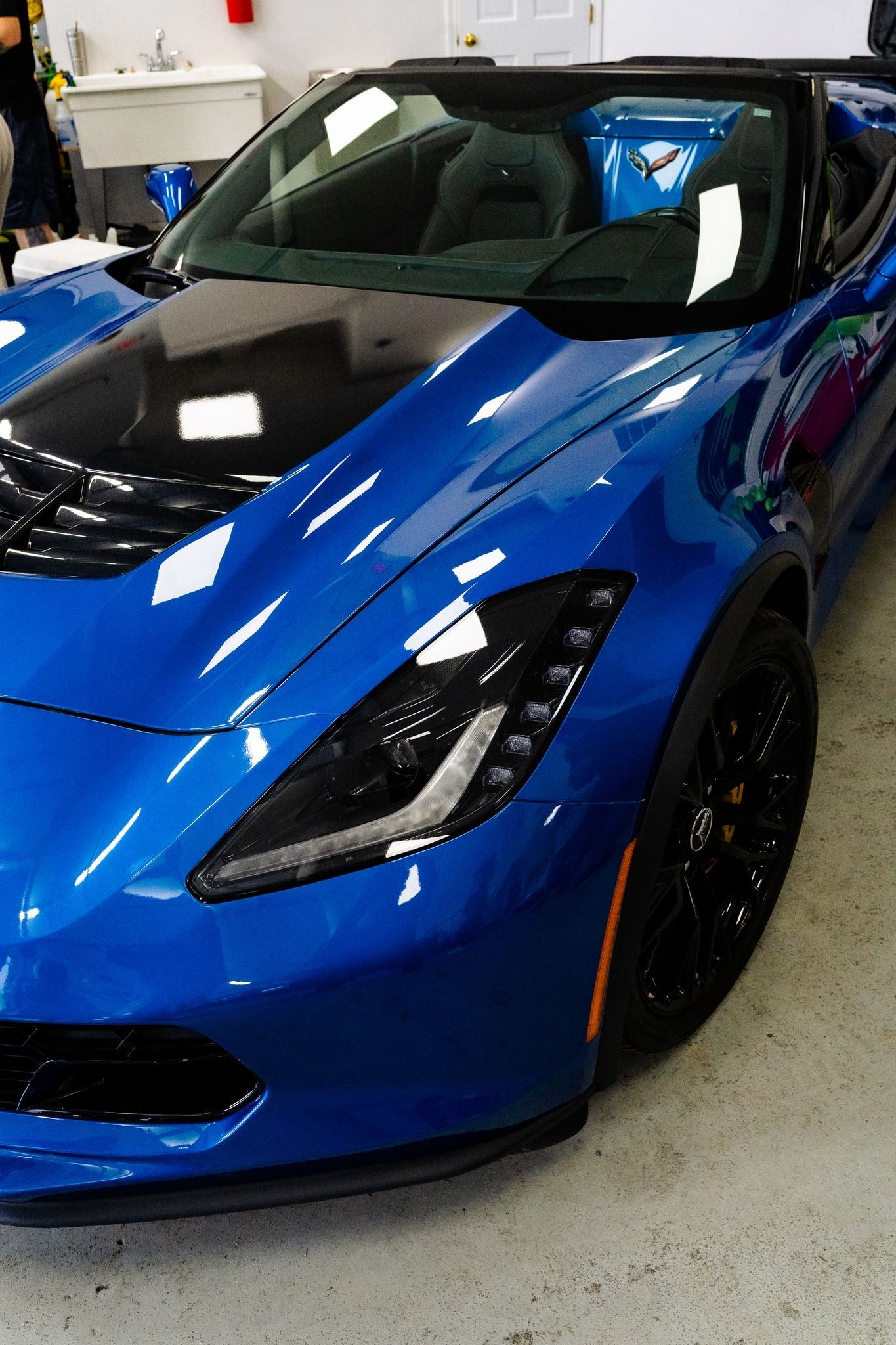 Blue sports car with a black hood and black wheels, indoors.