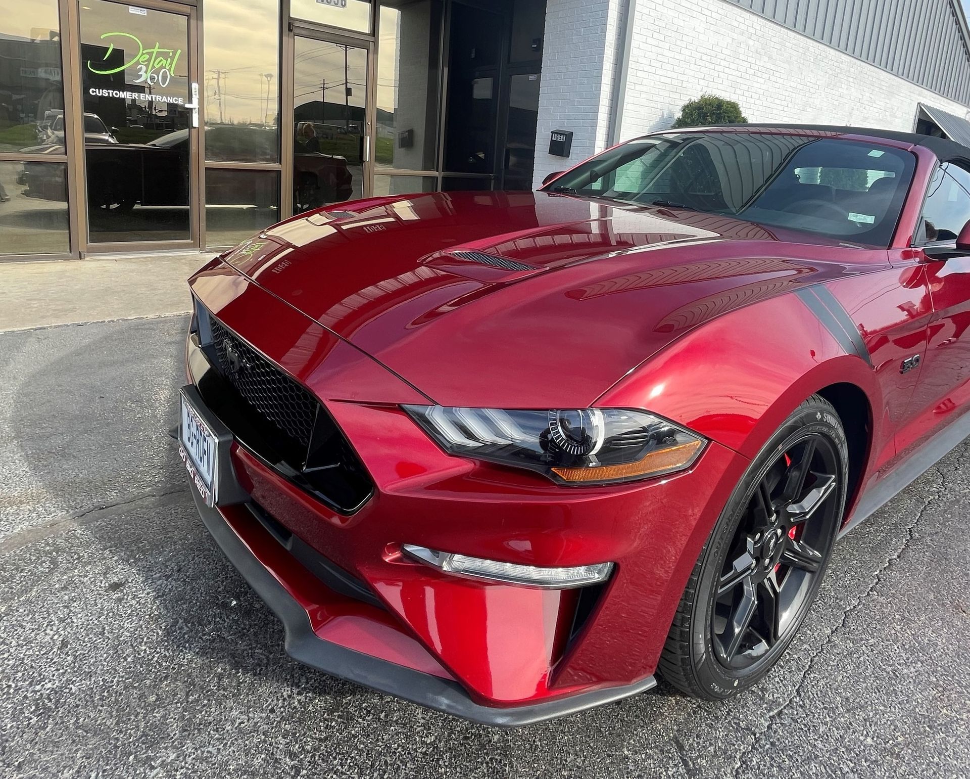 Red Ford Mustang convertible parked in front of a building with black racing stripes.