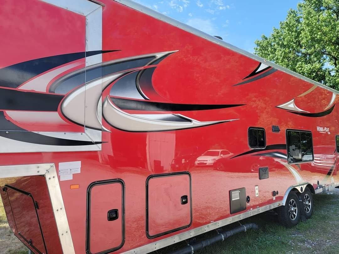 A red trailer with a black and white design is parked in the grass.