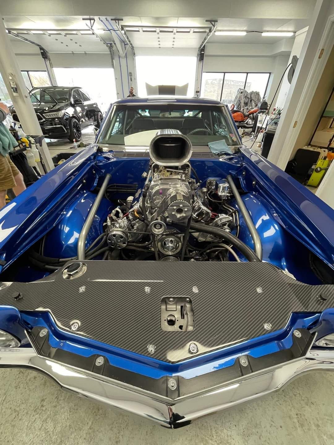 Blue classic car with chrome engine, hood scoop, and carbon fiber details.