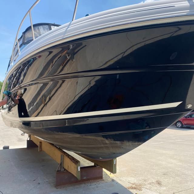 Black boat on wooden supports, reflecting sunlight. Outdoors, daytime.