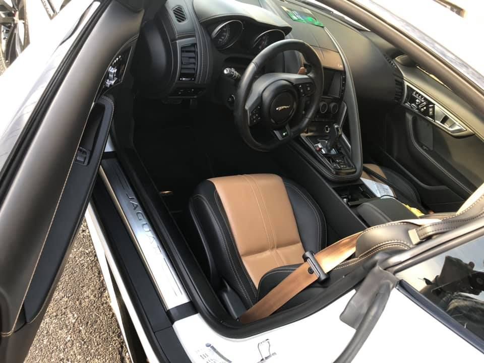 Interior of a white Jaguar sports car with black and tan leather seats and dashboard. The door is open.