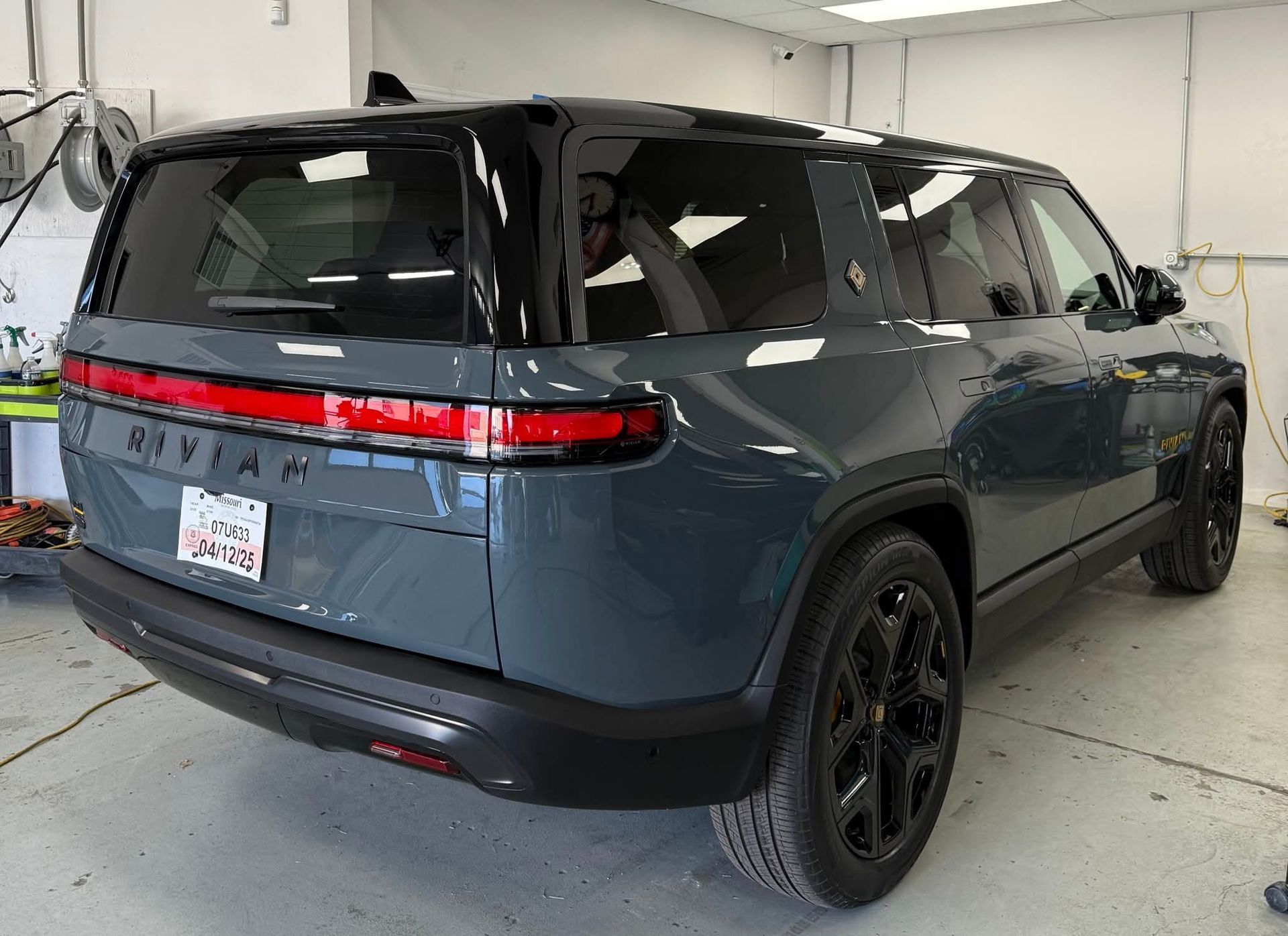 Dark blue Rivian SUV, black trim, tinted windows, in a garage. 