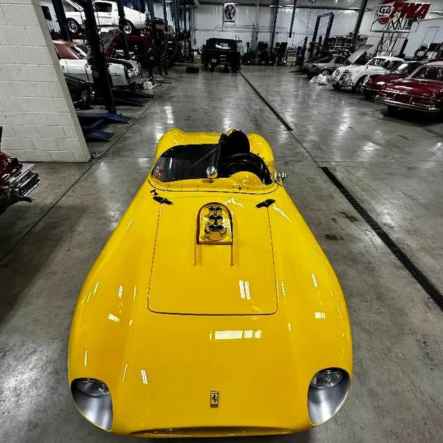 Yellow vintage sports car in a garage with other classic cars and mechanic equipment.
