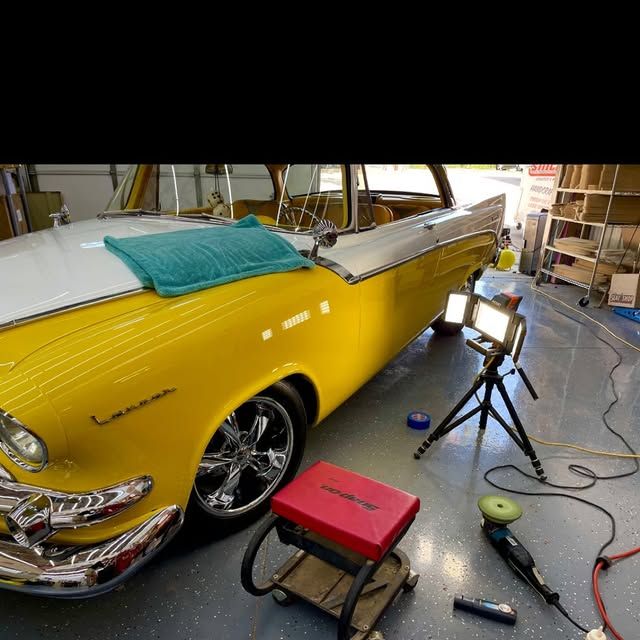 Yellow and white classic car being detailed in a garage; a work light and detailing equipment are nearby.