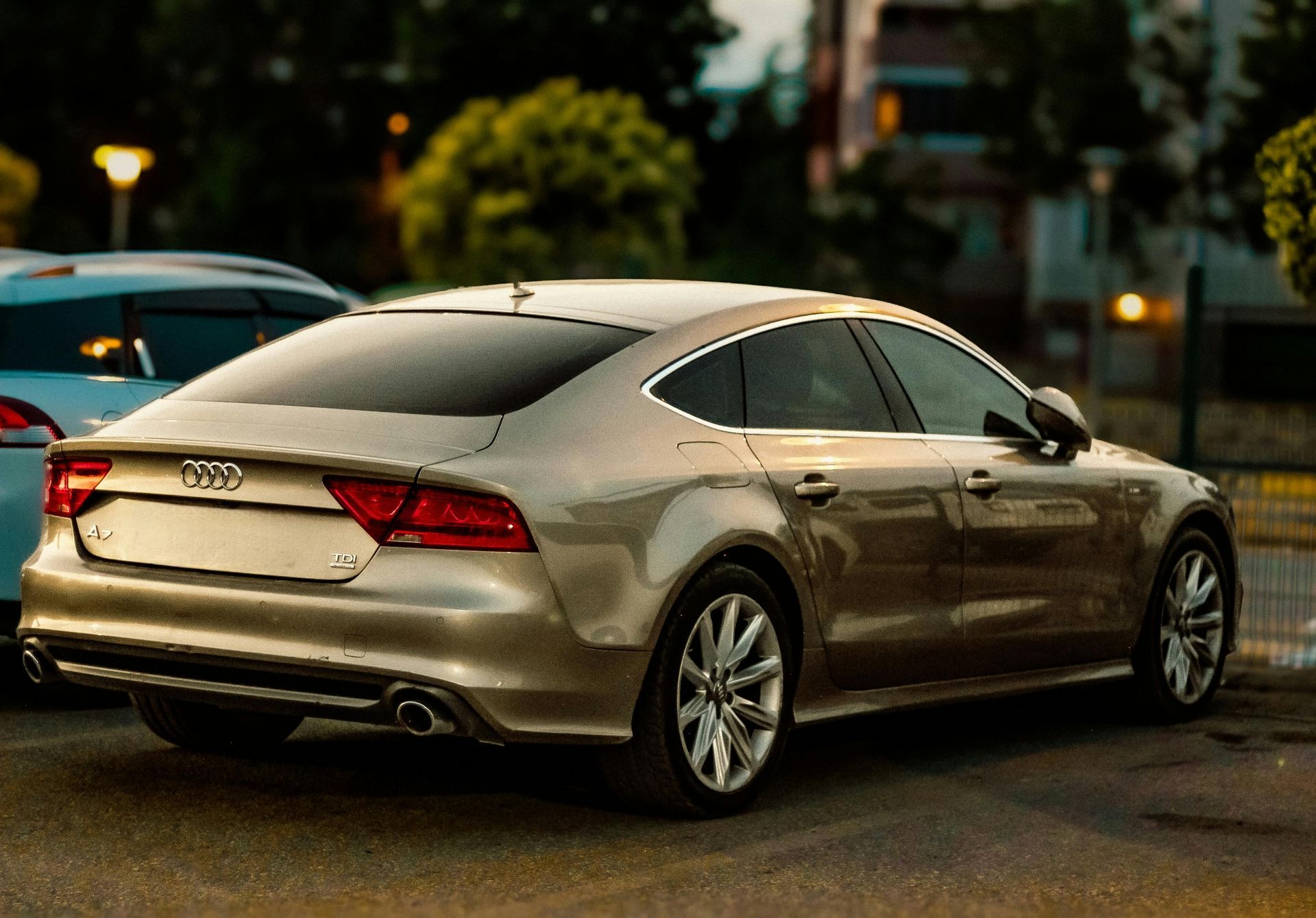 Gold Audi A7 sedan parked outdoors, evening lighting.