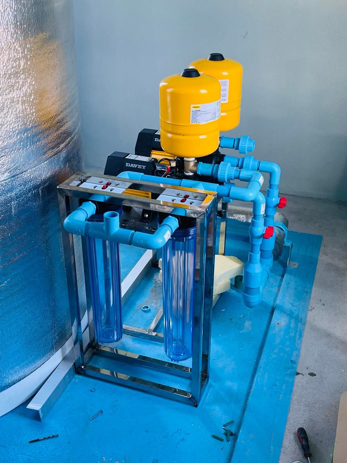 A water pump is sitting on top of a blue floor next to a tank.