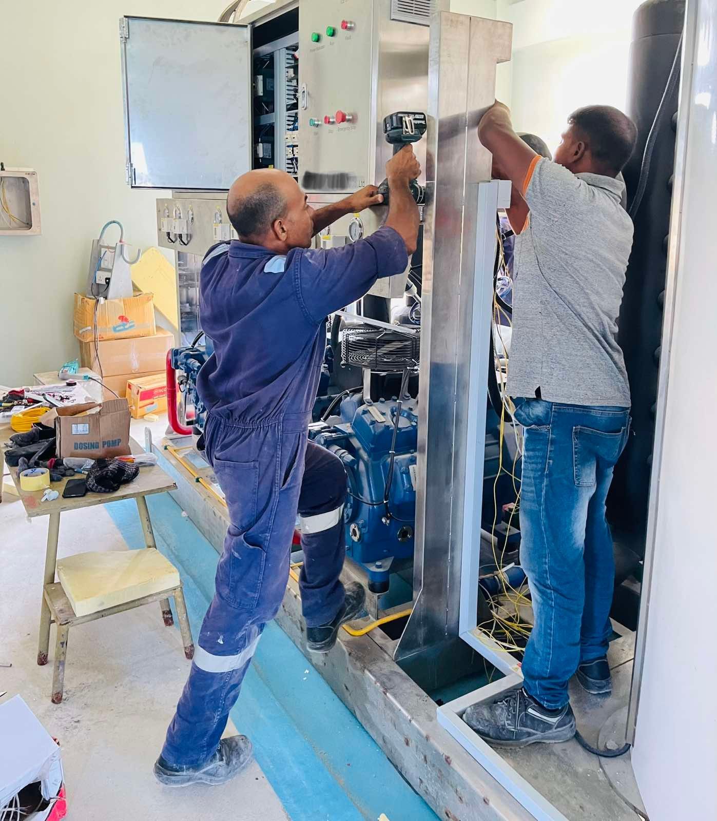 Two men are working on a machine in a room.