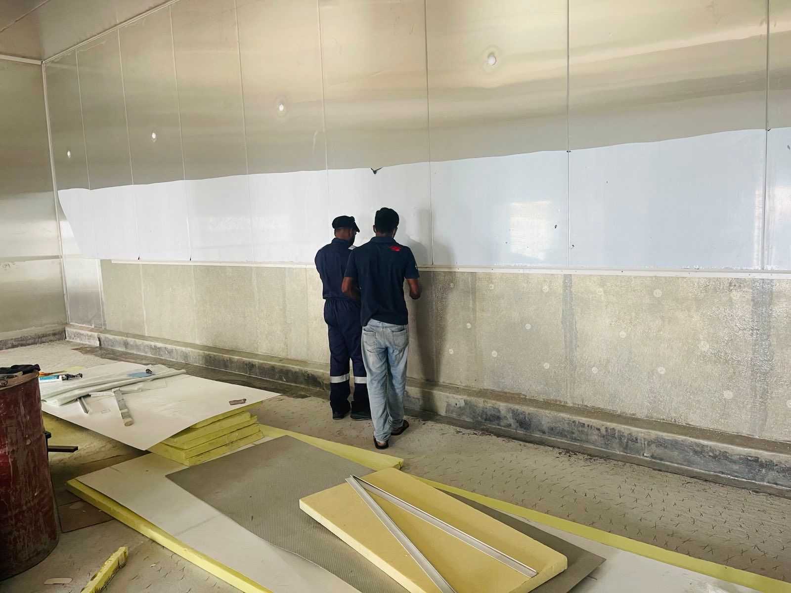 Two men are standing next to each other in a room looking at a wall.