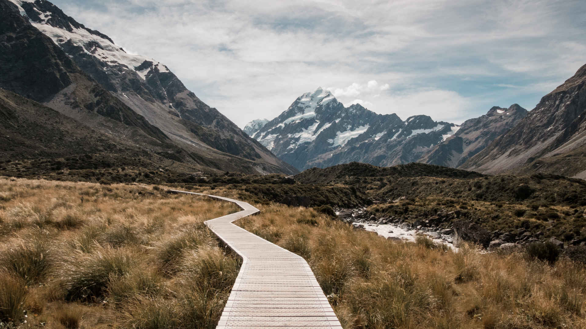 A wooden walkway leading to a mountain range with mountains in the background.