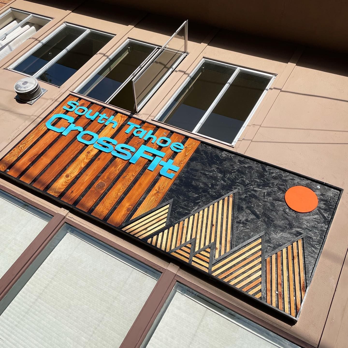 South Tahoe CrossFit sign on building exterior, blue text, wooden and abstract mountain design, orange sun.