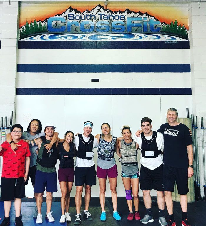 Group of people at South Tahoe CrossFit, posing together. Some wear vests. Background features mountains and logo.