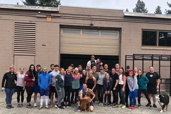 Group of people posing outside South Tahoe CrossFit gym with a dog. Many smiling, diverse ages and dressed in workout attire.